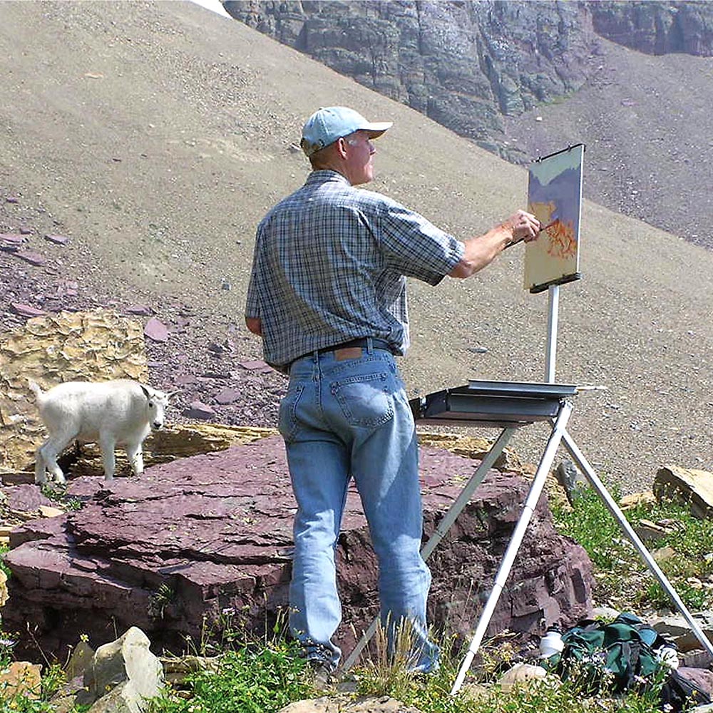 Artist Jim Wilcox paints on the Soltek Easel he designed for plein air painting on location in Glacier National Park with a mountain goat looking on